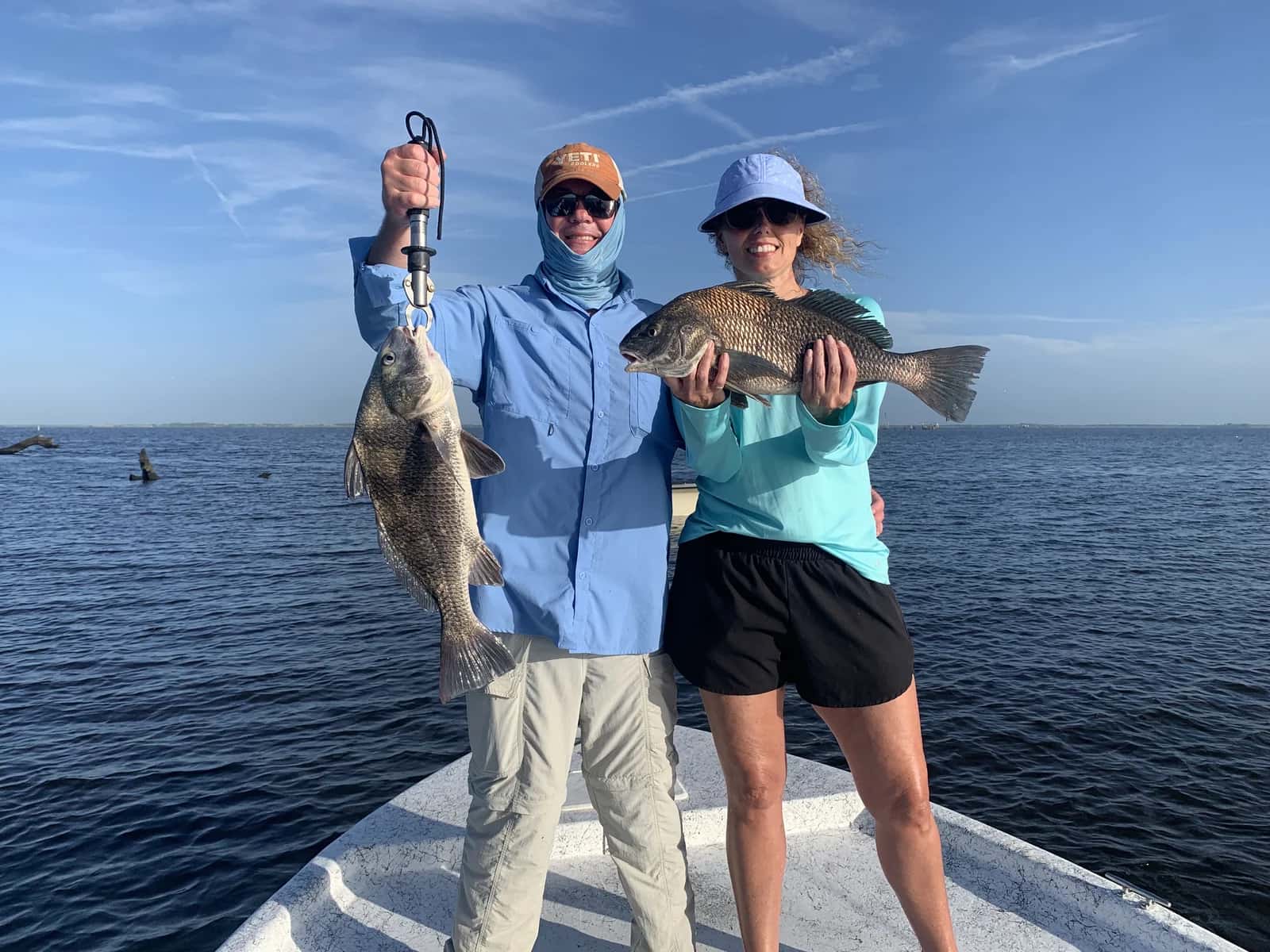 Two anglers displaying fish from the bow of the boat